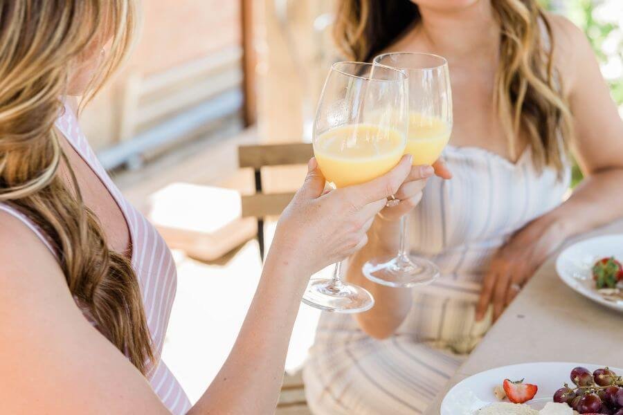 A lively photo of a group of young women, laughing and raising their mimosa-filled glasses in a cheerful toast during a vibrant brunch gathering.
